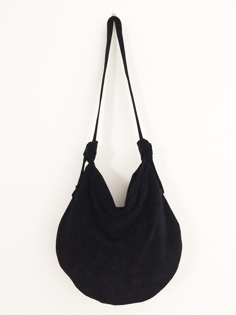 May include: A black, round, fabric tote bag with a long strap. The bag is made of a soft, textured fabric and has a gathered, slouchy look.