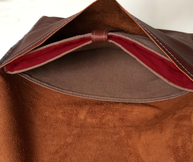 May include: A brown leather bag with a red lining and a suede interior. The bag is open and the lining is visible.