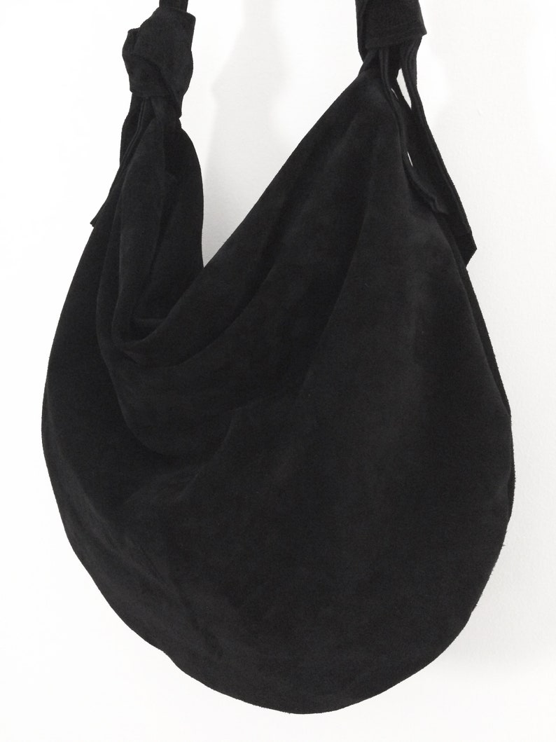 May include: A black suede hobo bag with a knotted strap and a slouchy design.