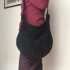 May include: A black suede shoulder bag with a long strap. The bag has a rounded shape and a knotted detail on the strap.