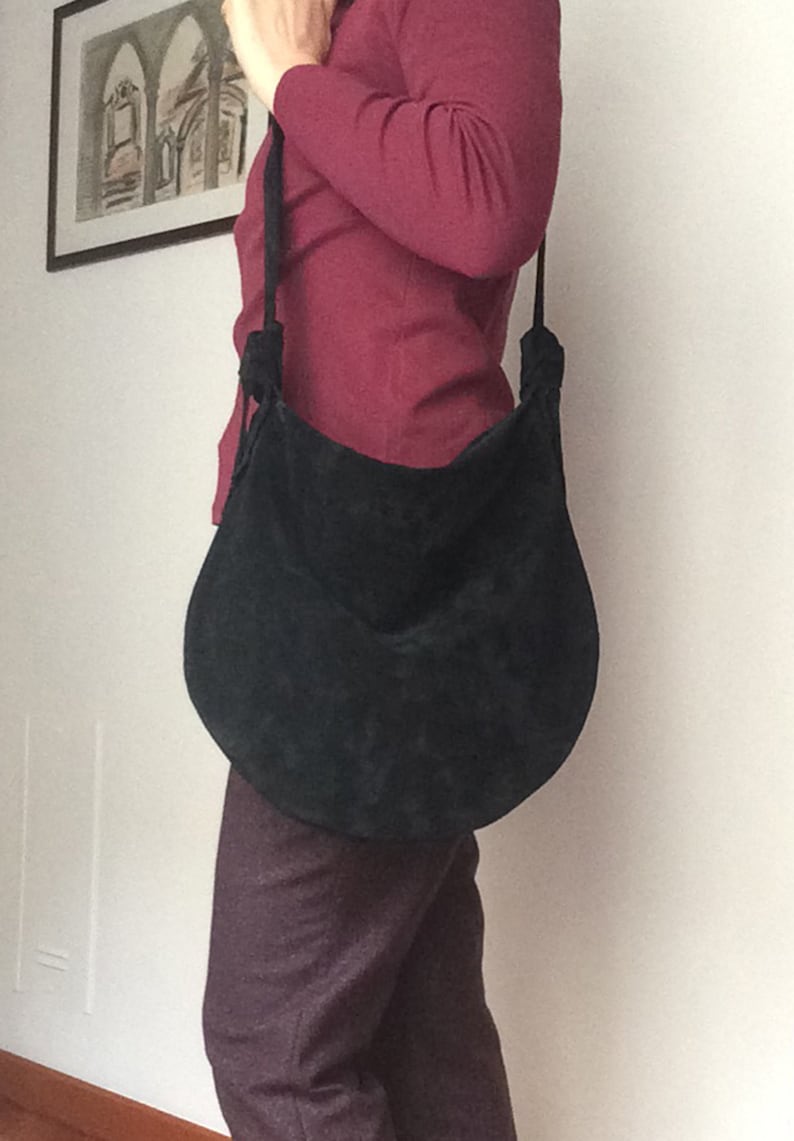 May include: A black suede shoulder bag with a long strap. The bag has a rounded shape and a knotted detail on the strap.