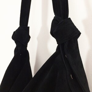May include: A black suede tote bag with two knotted straps and silver button accents.