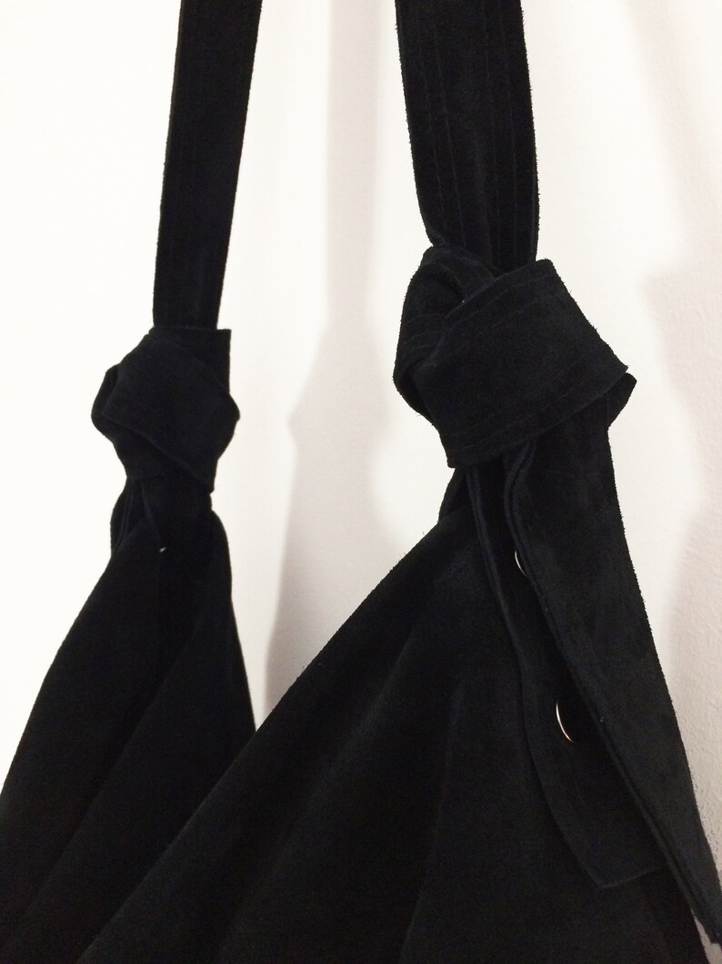 May include: A black suede tote bag with two knotted straps and silver button accents.
