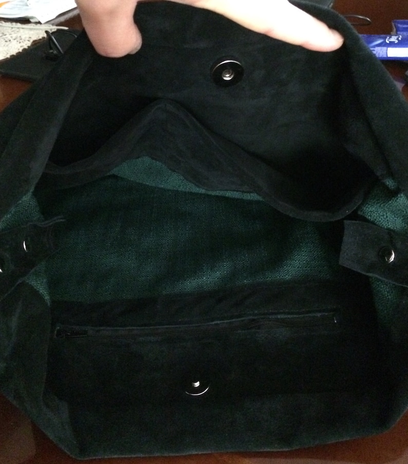 May include: Black suede tote bag with a green fabric lining and a zipped pocket. The bag has two snap closures.
