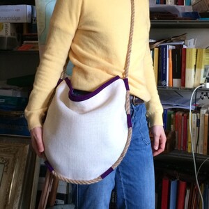 Peut inclure: Un sac en tissu blanc avec une bordure violette et une &eacute;paisse anse en corde. Le sac est port&eacute; en bandouli&egrave;re.