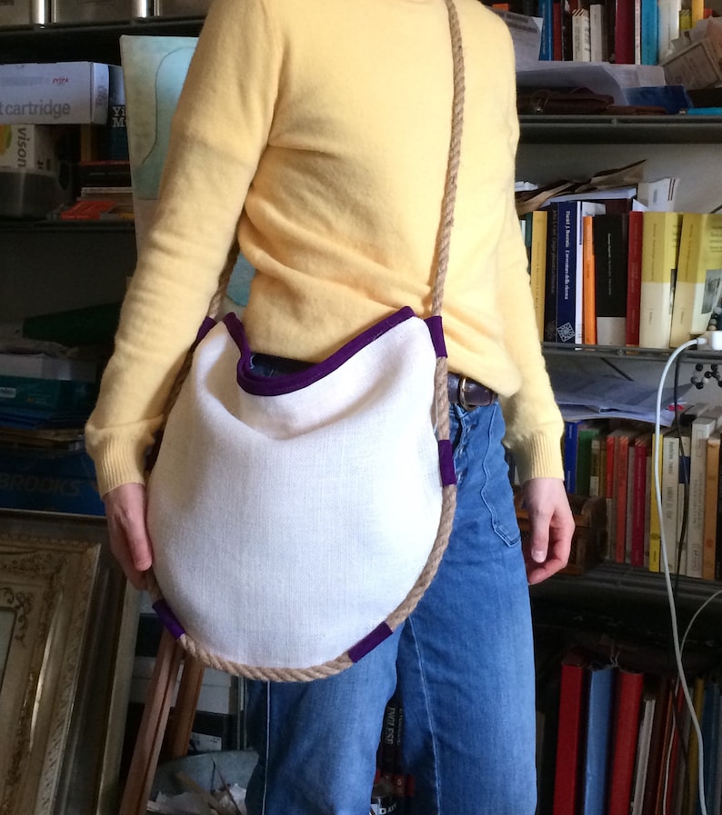 Peut inclure: Un sac en tissu blanc avec une bordure violette et une &eacute;paisse anse en corde. Le sac est port&eacute; en bandouli&egrave;re.