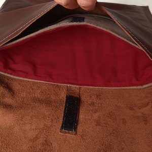 May include: A brown leather envelope with a red lining and a velcro closure. The envelope is open and the lining is visible.
