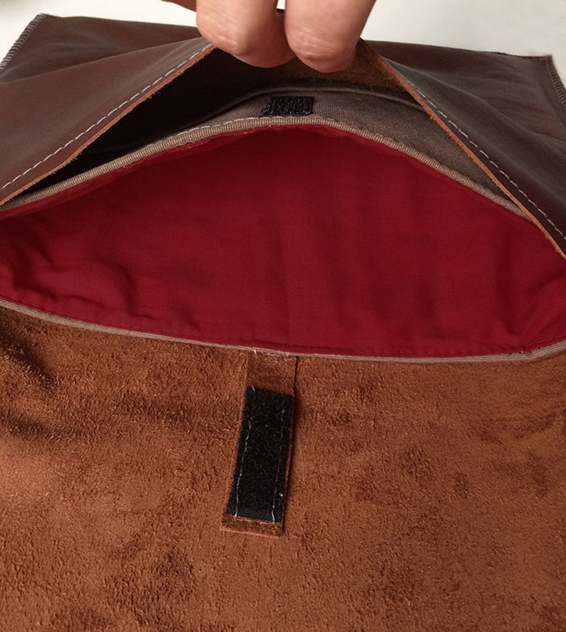 May include: A brown leather envelope with a red lining and a velcro closure. The envelope is open and the lining is visible.