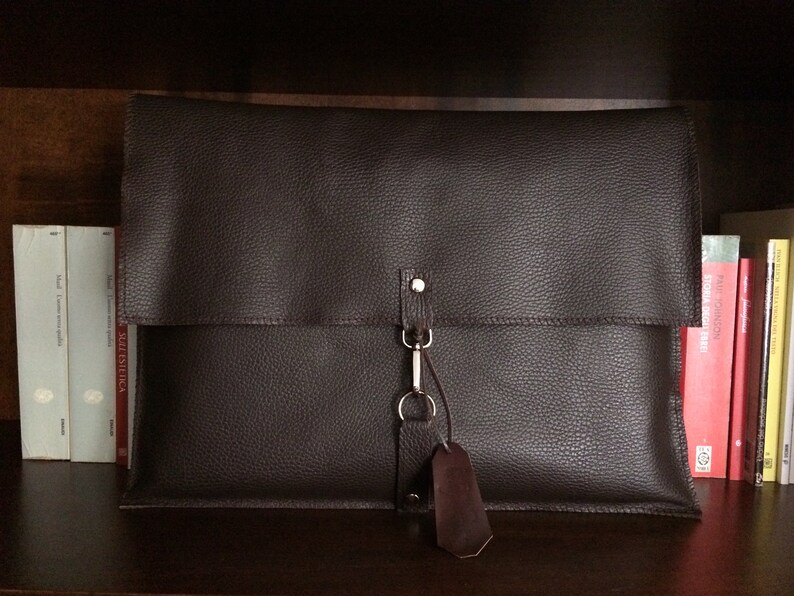 May include: A brown leather portfolio with a flap closure and a metal clasp. The portfolio has a key ring attached to it.