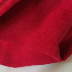 May include: Close-up of a red fabric with a smooth, velvety texture. The fabric is folded and has a slight sheen.
