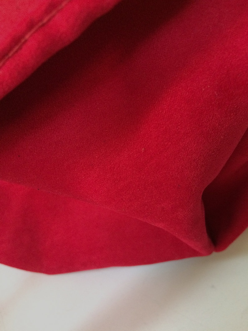 May include: Close-up of a red fabric with a smooth, velvety texture. The fabric is folded and has a slight sheen.