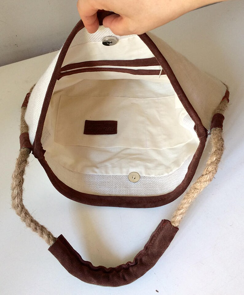 Peut inclure: Un sac cabas en toile blanche avec des anses en corde marron et une bordure en daim marron. Le sac a une poche int&eacute;rieure en tissu marron.