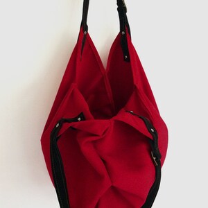 May include: A red canvas tote bag with black straps and a buckle closure. The bag is empty and turned inside out.