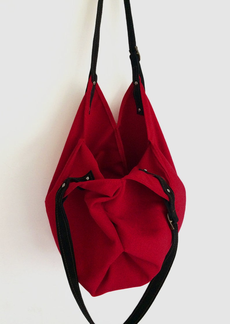 May include: A red canvas tote bag with black straps and a buckle closure. The bag is empty and turned inside out.