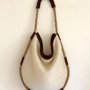 Peut inclure: Un sac fourre-tout en toile blanche avec des finitions en cuir marron et des anses en corde.