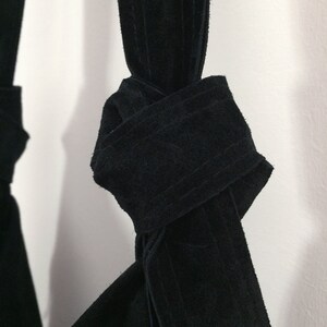 May include: A black suede bag with a knotted strap. The strap is tied in a knot at the top of the bag.
