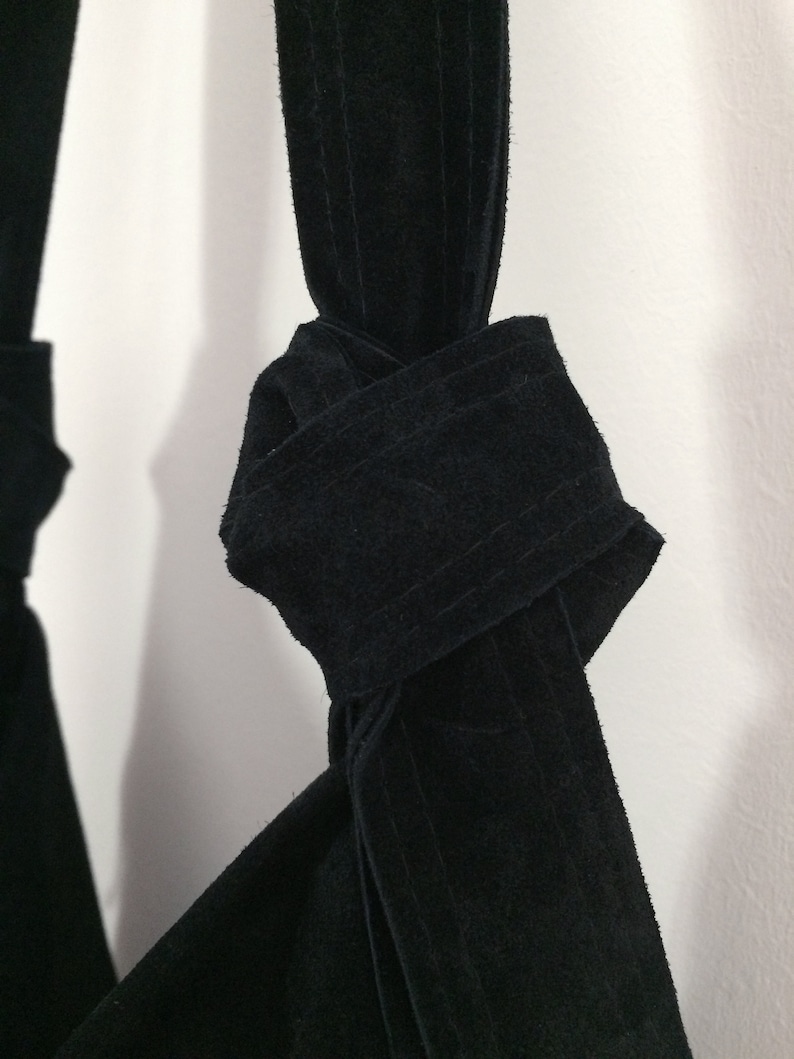 May include: A black suede bag with a knotted strap. The strap is tied in a knot at the top of the bag.