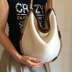 Peut inclure: Un sac cabas en toile blanche avec des finitions en cuir marron et une &eacute;paisse poign&eacute;e en corde. Le sac est grand et spacieux, et il serait parfait pour transporter les essentiels du quotidien.