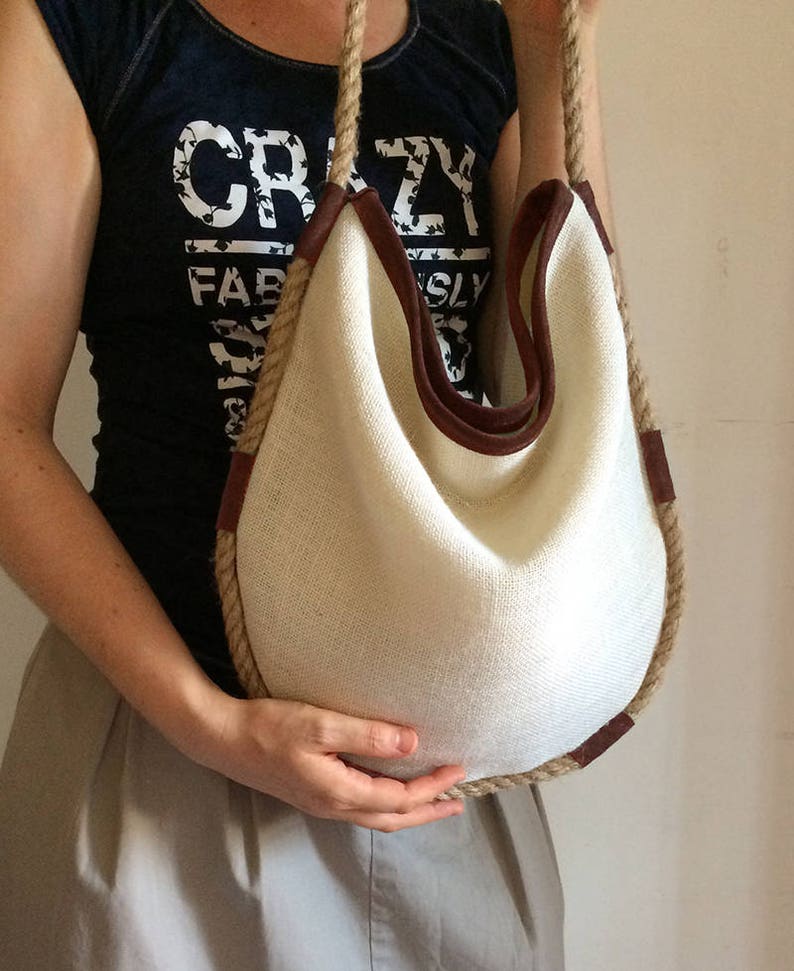 Peut inclure: Un sac cabas en toile blanche avec des finitions en cuir marron et une &eacute;paisse poign&eacute;e en corde. Le sac est grand et spacieux, et il serait parfait pour transporter les essentiels du quotidien.