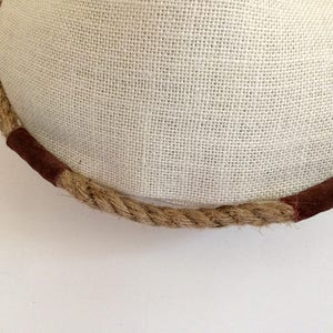 Peut inclure: Gros plan sur une garniture en corde brune avec deux accents en cuir brun. La corde est enroul&eacute;e autour d'une surface en tissu blanc.