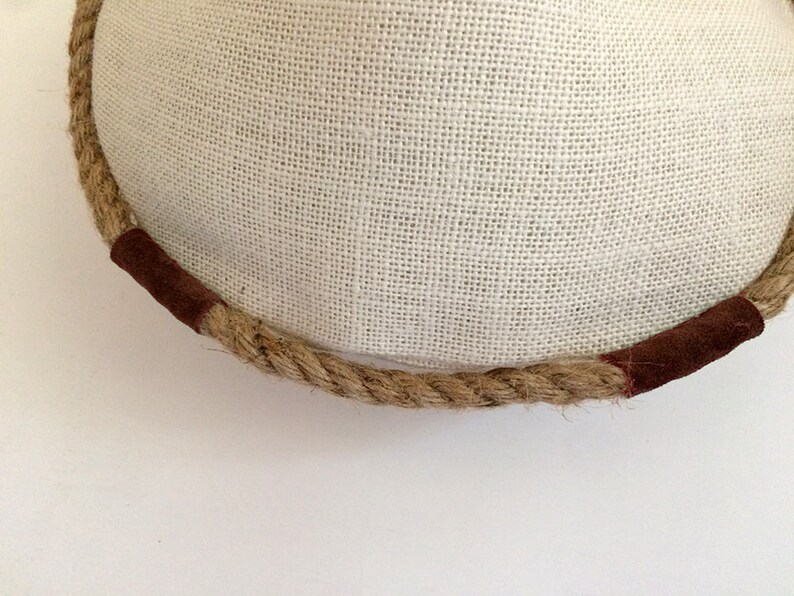 Peut inclure: Gros plan sur une garniture en corde brune avec deux accents en cuir brun. La corde est enroul&eacute;e autour d'une surface en tissu blanc.