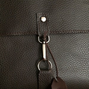 May include: A brown leather bag with a silver metal clasp and a brown leather strap. The bag has a textured surface.