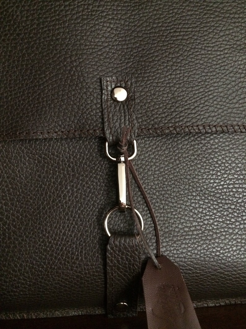 May include: A brown leather bag with a silver metal clasp and a brown leather strap. The bag has a textured surface.