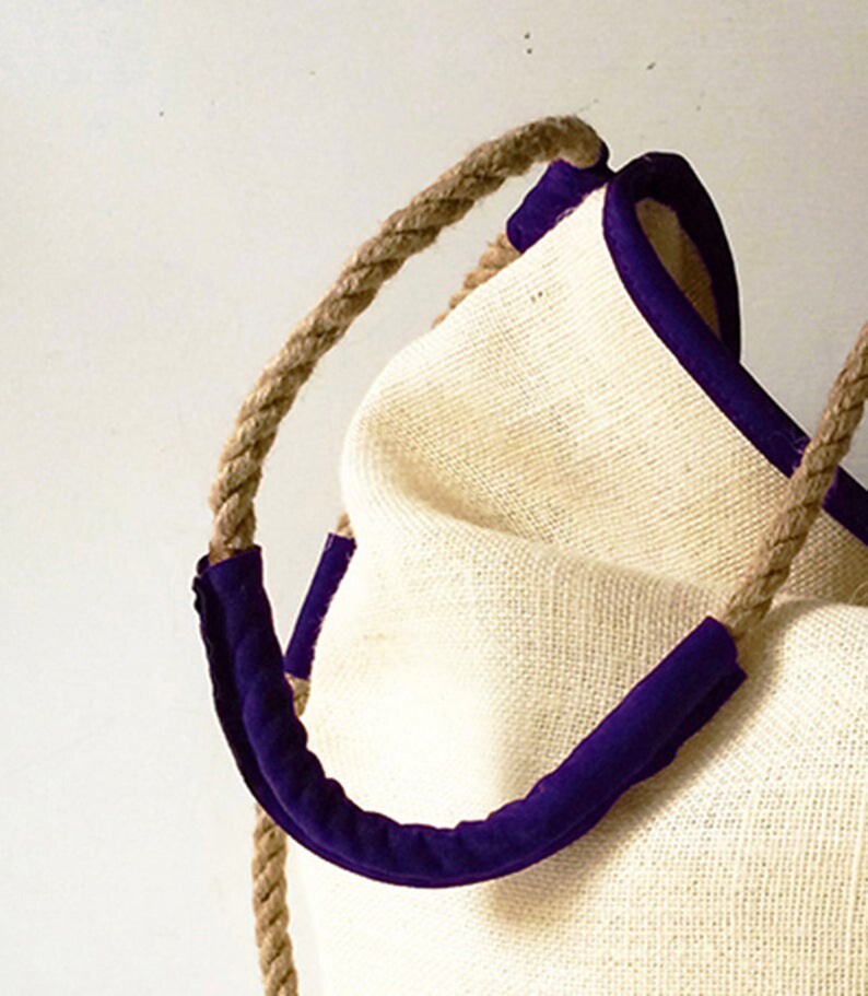 Peut inclure: Un sac fourre-tout en fibre naturelle avec une bordure violette et des anses en corde.