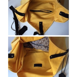 May include: A yellow canvas tote bag with black leather straps and a small zippered pocket inside. The bag has a black leather tag with the word "Genuine" on it.