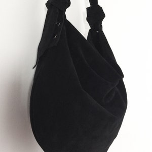 May include: A black, round, fabric tote bag with a knotted strap. The bag has a gathered, loose, and slouchy look.