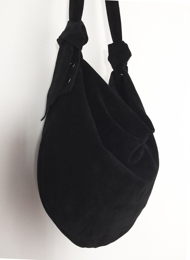 May include: A black, round, fabric tote bag with a knotted strap. The bag has a gathered, loose, and slouchy look.