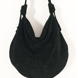 May include: A black suede hobo bag with knotted straps.