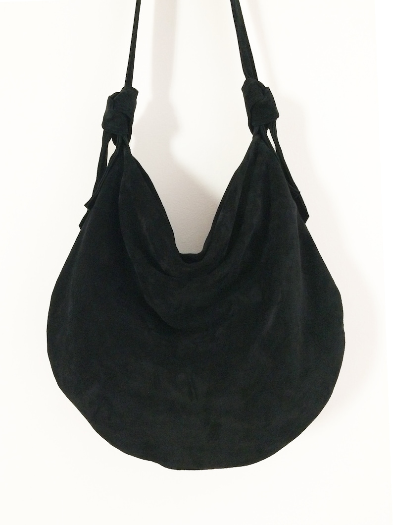 May include: A black suede hobo bag with knotted straps.