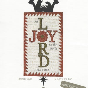 May include: A Christmas quilt pattern featuring the text "Joy to the World" and "The Lord has come!" in a decorative font. The design includes a silhouette of a nativity scene and measures 31.75 cm x 54.61 cm.