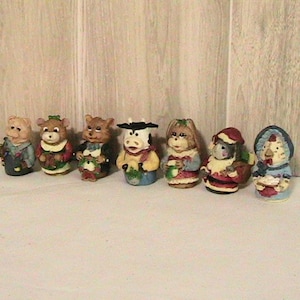 May include: A collection of seven small, decorative figurines. The figurines depict various animals, including bears, a cow, and a chicken, dressed in festive attire. The figurines are painted with detailed features and vibrant colors, perfect for holiday decor.