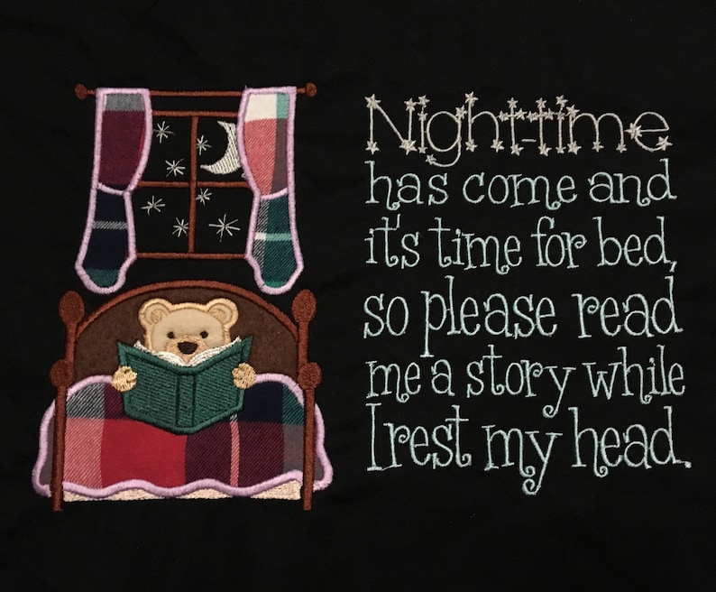 May include: Embroidered design on a black fabric featuring a teddy bear in a bed with a book and the text "Nighttime has come and it's time for bed, so please read me a story while I rest my head."