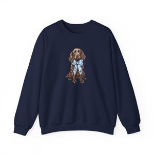 May include: A navy blue sweatshirt with a brown and white dog wearing a blue and white bow tie. The dog is sitting and looking to the right.