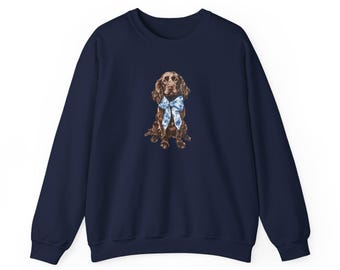 May include: A navy blue sweatshirt with a brown and white dog wearing a blue and white bow tie. The dog is sitting and looking to the right.
