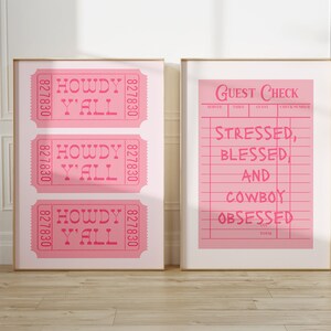 May include: Two framed prints with gold frames. One print features three pink tickets with "HOWDY Y'ALL" text. The other print is a pink guest check with the text "STRESSED, BLESSED AND COWBOY OBSESSED".