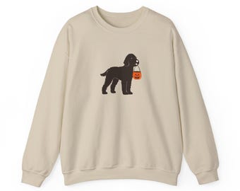 Puede incluir: Sudadera beige con una ilustración de un perro negro que lleva un cubo de calabaza naranja. La parte superior de manga larga es de color neutro, adecuada para uso informal. El gráfico del perro es un diseño sencillo, de estilo caricatura, perfecto para Halloween.