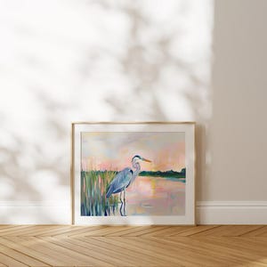 May include: A painting of a blue heron standing in a marsh at sunset. The heron is facing to the right and has its head turned to the left. The water is a light pink color and the sky is a light blue color. The marsh is a dark green color.