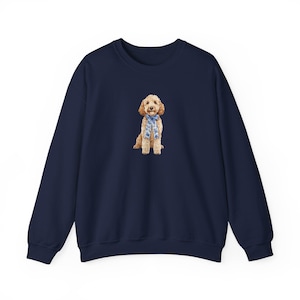 May include: A navy blue sweatshirt featuring a watercolor illustration of a golden doodle dog wearing a blue patterned scarf. The dog is centered on the front of the long-sleeved crew neck top. The sweatshirt is made of a soft material.