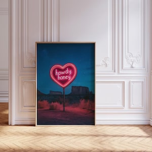 May include: A neon pink heart-shaped sign with the words "howdy honey" in a desert landscape under a starry night sky.