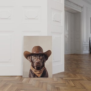 Könnte beinhalten: Ein brauner Labrador Retriever, der einen braunen Cowboyhut und ein braunes Bandana trägt. Der Hund schaut direkt in die Kamera.