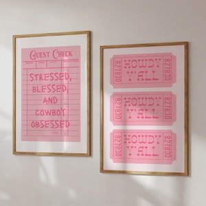 May include: Two framed pink prints with gold frames. One print reads "Guest Check" with the text "Stressed, Blessed, and Cowboy Obsessed." The other print features three pink tickets that read "Howdy Y'all."