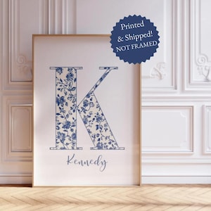May include: A rectangular wall art print featuring a large capital letter K filled with a blue and white floral pattern. Below the letter, the name Kennedy is written in a blue script font. A dark blue circular badge states Printed & Shipped! NOT FRAMED.