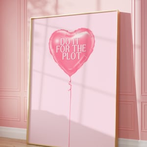 May include: A pink heart-shaped balloon with the text "DO IT FOR THE PLOT" printed on it. The balloon is tied with a pink ribbon and is floating against a light pink background.