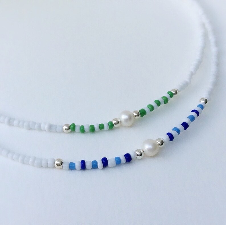 May include: Two delicate necklaces with white beads and a pearl accent. One necklace features green and white beads, while the other has blue and white beads.