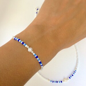 May include: A white and blue beaded bracelet and necklace set with a pearl accent on each piece.