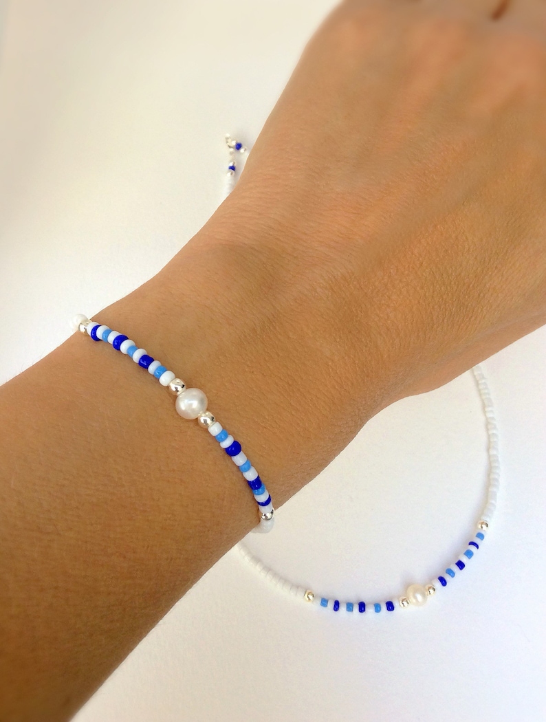 May include: A white and blue beaded bracelet and necklace set with a pearl accent on each piece.